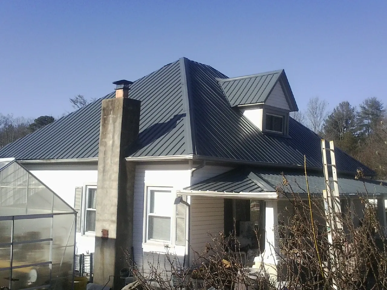 Dark blue standing seam metal roof on a white farmhouse with dormer — Slate & Tile Roof Repair by Roofing Brothers in Seaboard