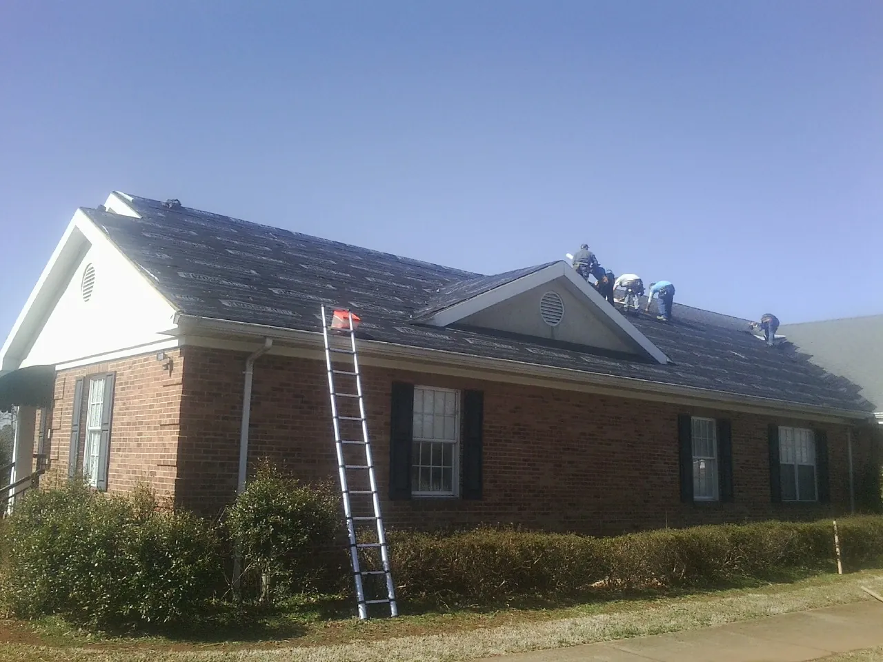 Crew tearing shingles off a brick ranch roof with a ladder set — Emergency Roof Repair work by our crew in Seaboard