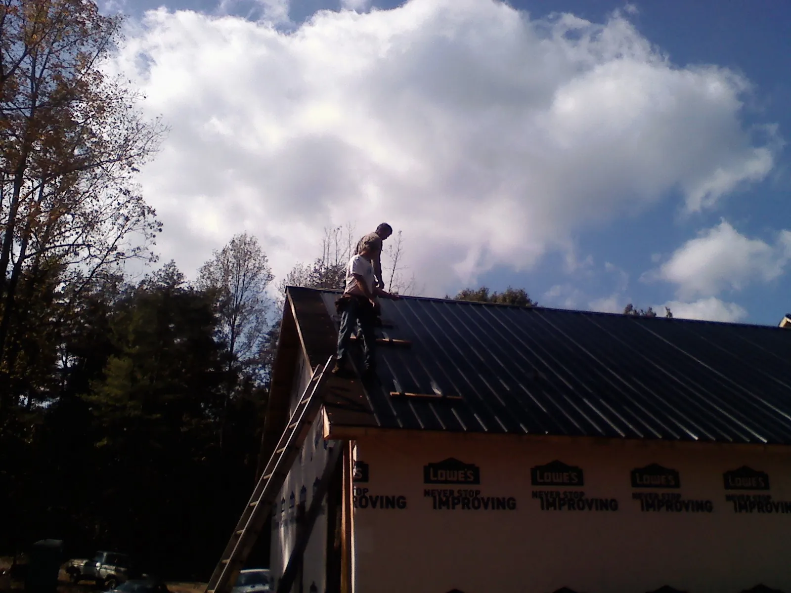 Roofer fastening dark metal panels high against a cloudy sky, from a Roof Inspection job in Seaboard