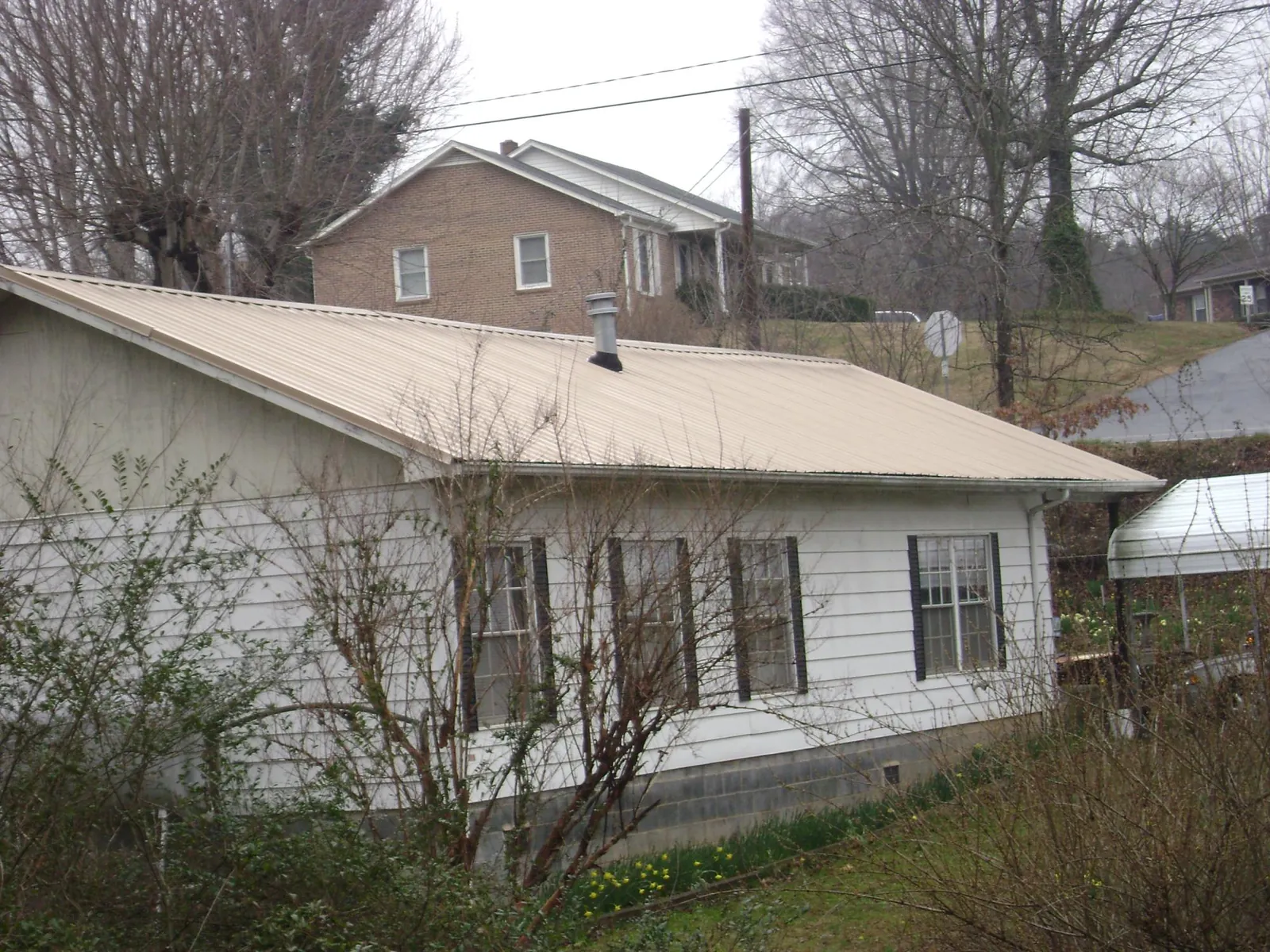Tan metal roof on a white sided house set into a hillside — Commercial Roofing by Roofing Brothers in Seaboard