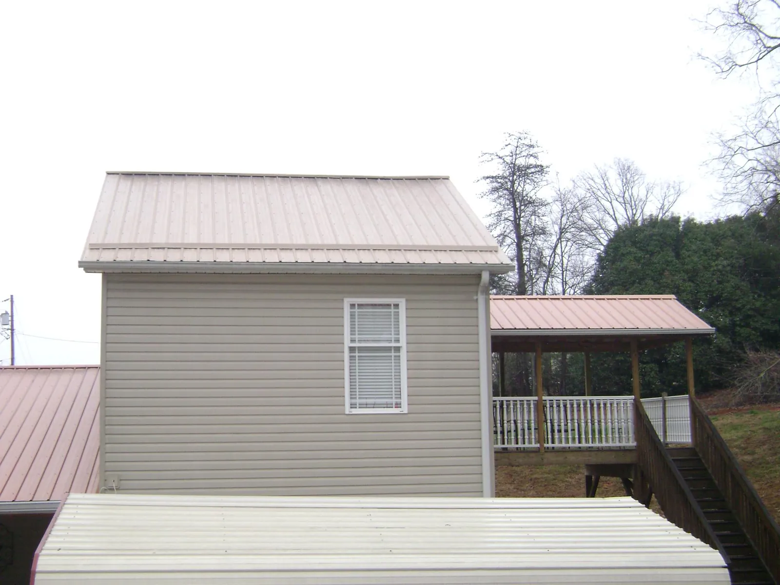 Tan metal roofs on a two story addition and attached porch, from a Roof Replacement job in Seaboard